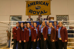 A group of people standing in front of an American Royal banner, showcasing Hereford shows.