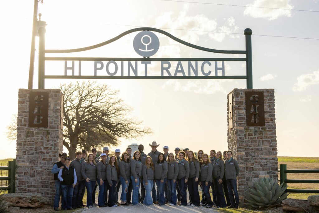 A group of people standing in front of a sign that says Hi Point Ranch, where Herefords and Production Cattle Sales take place.